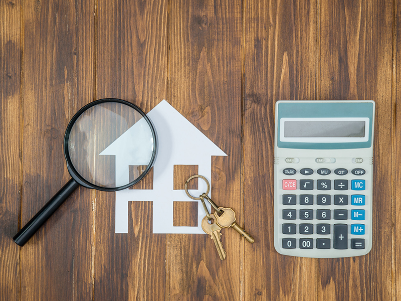 Photo of magnifying glass over image of house with keys next to a calculator