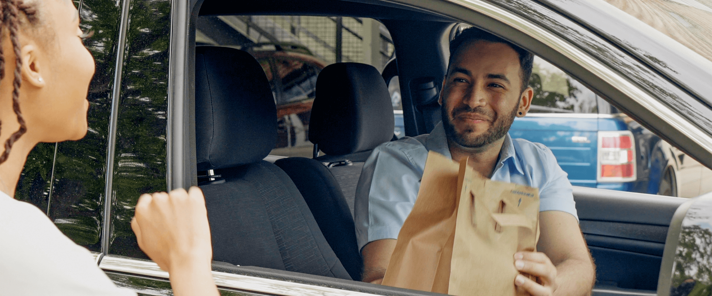 Smiling man in his 30s receives grocery bag through his car window