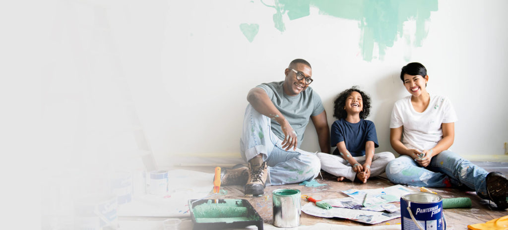 A family sitting in front of a wall that they are painting